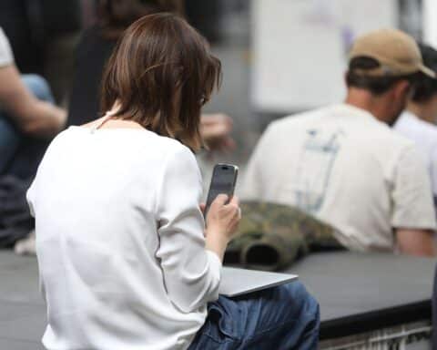 Frau mit Smartphone, Fokus auf Selfie-Kamera, moderne Technik und deren Bedeutung für Nutzer.