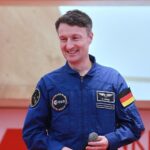 Matthias Maurer mit Raumanzug vor einer Mondlandschaft; symbolisiert Deutschlands Mondmission.