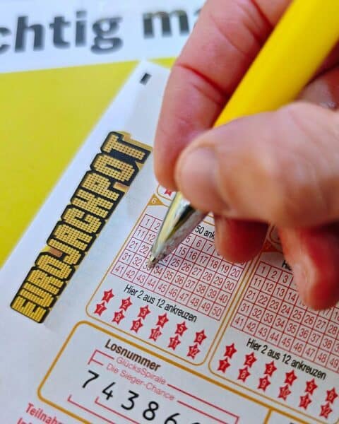 Ein Eurojackpot-Spielschein mit Gewinnzahlen und symbolischen Eurozeichen im Hintergrund.