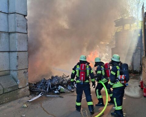 Feuerwehr im Einsatz gegen großen Brand in Recyclingbetrieb; Rauch und gebranntes Material sichtbar.