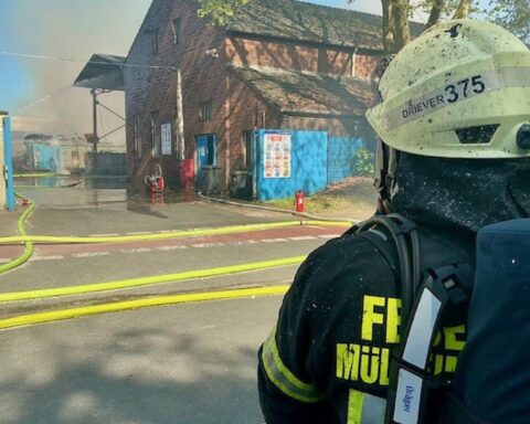 Großbrand mit Rauchsäule, Feuerwehr im Einsatz, brennende Altpapierballen, Verletzter, dramatische Szene.