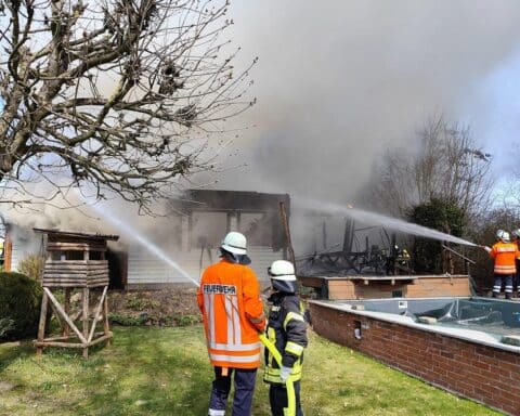 Rauchentwicklung vom brennenden Holzhaus, Feuerwehr im Einsatz, Anwohner warnen.