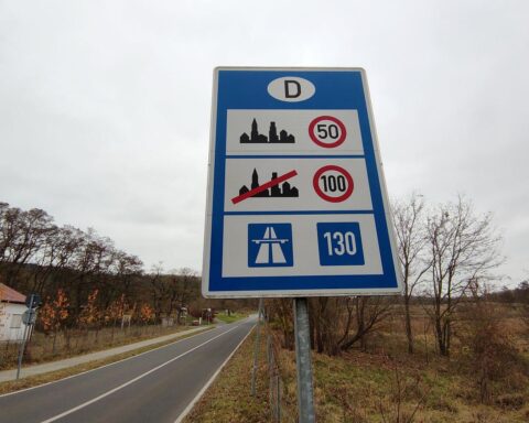 Verkehrsschild mit Geschwindigkeitsbegrenzung, Autos auf der Autobahn und Sicherheitshinweise.