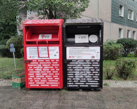 Sammelcontainer für Altkleider in einer Stadt, umgeben von Vegetation, Symbol für Recycling.