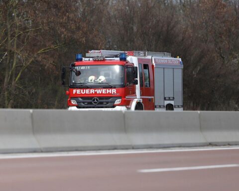 Feuerwehrlöscharbeiten an brennendem Gebäude mit Schäden an Fahrzeug und angrenzenden Objekten.