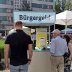Passanten informieren sich am Infostand über Bürgergeld und Krankenkassenfinanzierung in Berlin.