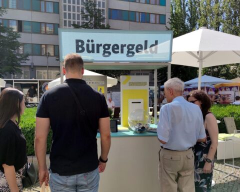 Passanten informieren sich am Infostand über Bürgergeld und Krankenkassenfinanzierung in Berlin.