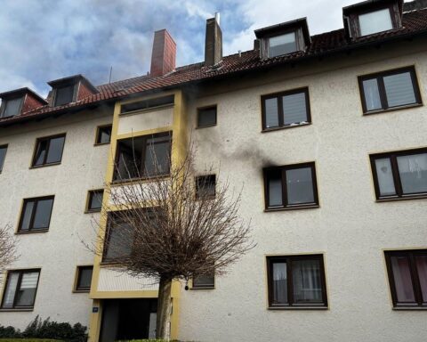 Feuerwehr im Einsatz gegen Küchenbrand in Bremerhaven, Rauch dringt aus einem Fenster.