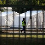 Flüchtling und Sicherheitsmann in einer Zeltstadt, Symbol für Integration und Unterstützung.