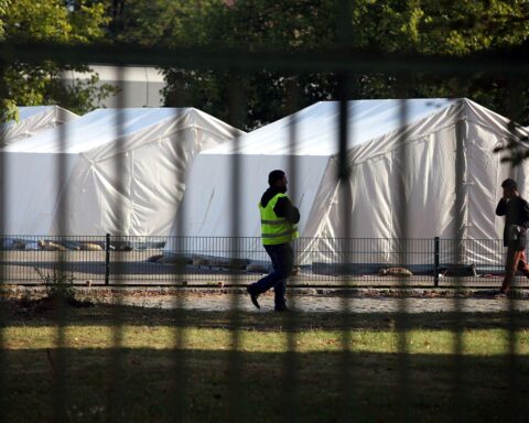 Flüchtling und Sicherheitsmann in einer Zeltstadt, Symbol für Integration und Unterstützung.