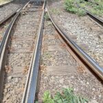 Bahnarbeiter bauen an Rail Baltica, während Sicherheitskräfte militärische Infrastruktur überwachen.