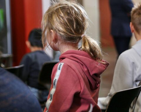 Kinder in Schule, besorgt über Kürzungen; Symbol für Schwächere in Gesellschaftsbus.