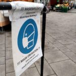 Einsame Menschen auf Wochenmarkt mit Masken, symbolisieren die Auswirkungen von Long Covid und ME/CFS.