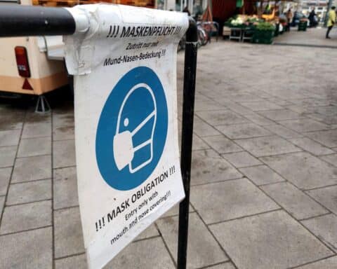 Einsame Menschen auf Wochenmarkt mit Masken, symbolisieren die Auswirkungen von Long Covid und ME/CFS.