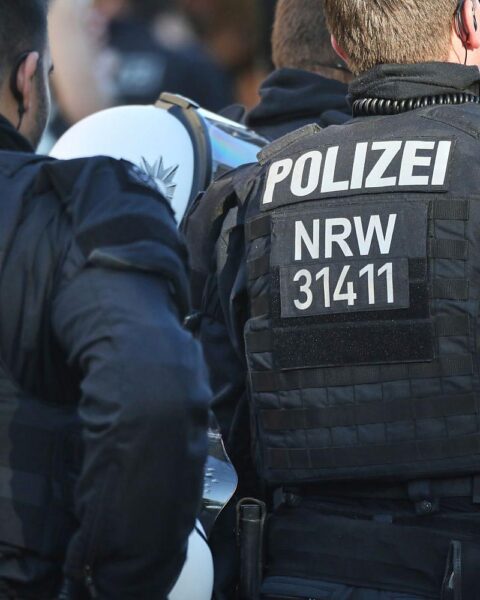 Ein Polizist untersucht eine blutige Tatstelle mit verletztem Mann und Ermittlern in der Nähe.