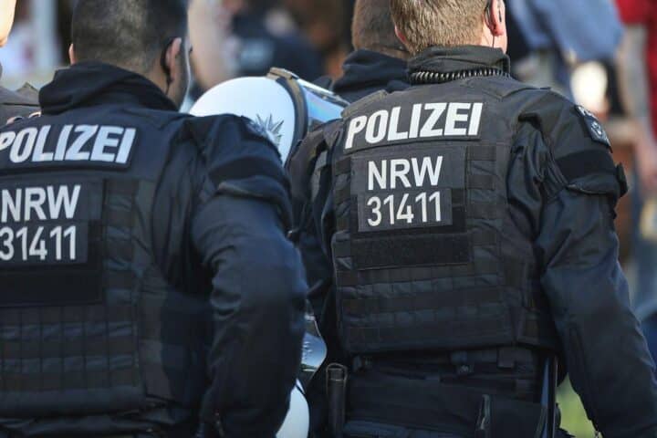 Ein Polizist untersucht eine blutige Tatstelle mit verletztem Mann und Ermittlern in der Nähe.