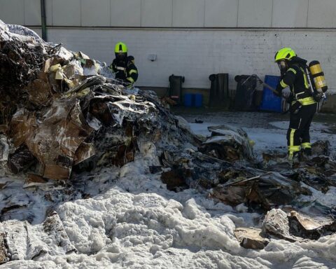 Feuerwehr löscht brennende Müllpresse in Gewerbebetrieb; rauchende Flammen und Löscharbeiten sichtbar.