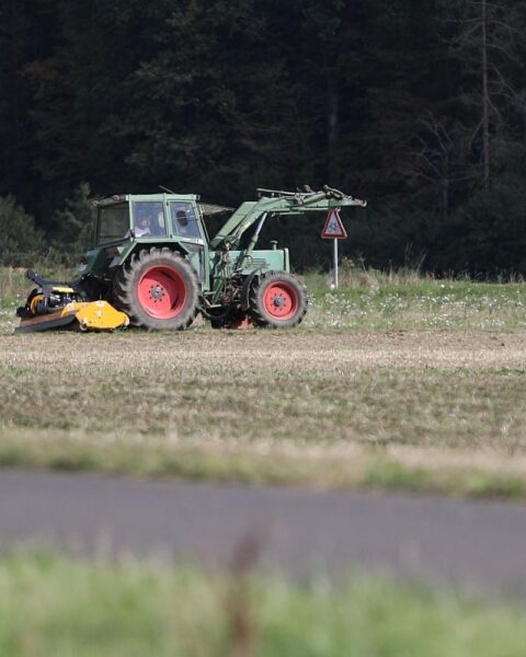 Ein Bauer fährt mit Traktor über ein Feld voller Düngemittel und Pflanzen.