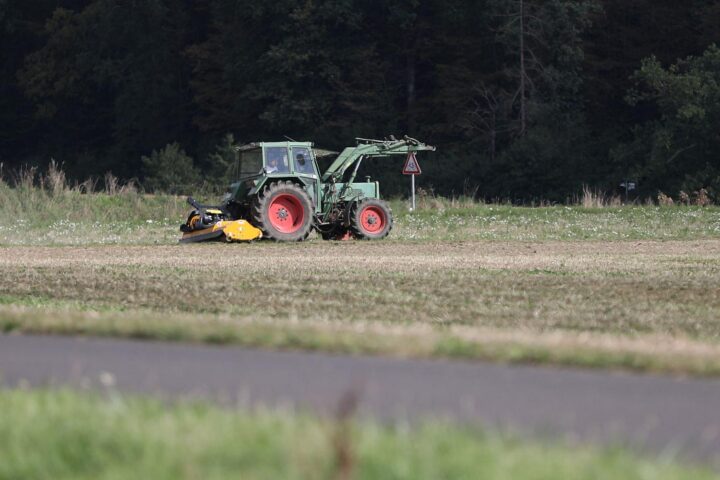 Ein Bauer fährt mit Traktor über ein Feld voller Düngemittel und Pflanzen.