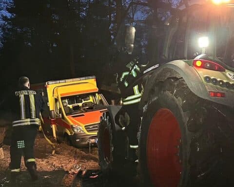 Traktor zieht steckengebliebenes Einsatzfahrzeug aus matschigem Waldweg, Feuerwehr im Einsatz.