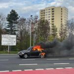 Brennender VW Käfer auf der Straße, Feuerwehr im Einsatz, starke Rauchentwicklung sichtbar.