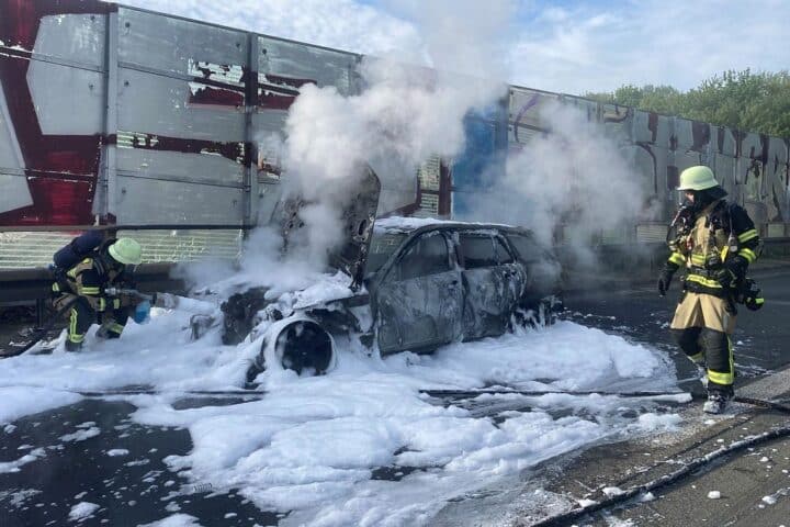 Auto in Flammen, Feuerwehr im Einsatz, dichte Rauchentwicklung, Rettungsgasse auf Autobahn sichtbar.