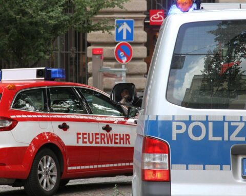 Ein Feuerwehrteam am Unfallort mit einem verunglückten Ultraleichtflugzeug im Hintergrund.