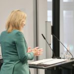 Nina Warken diskutiert Gesundheitsreform, umgeben von politischen Beratern und kritischen Stimmen.