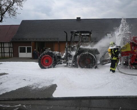 Traktorbrand auf Straße, Feuerwehr im Einsatz, Qualm und Flammen sichtbar, Schadensmeldung.