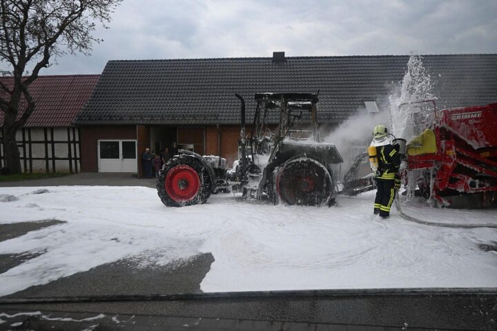 Traktorbrand auf Straße, Feuerwehr im Einsatz, Qualm und Flammen sichtbar, Schadensmeldung.