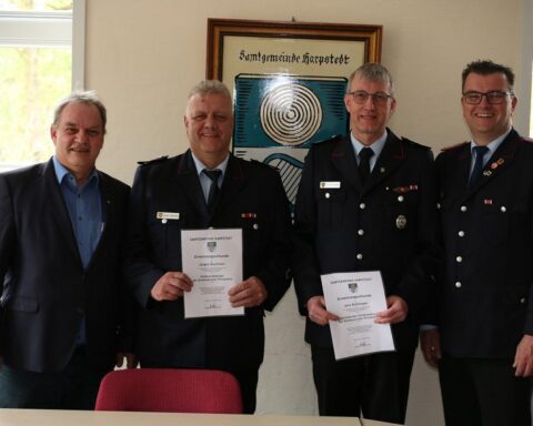 Feierliche Ernennung von Feuerwehrführern mit Bürgermeistern und Gratulationen, Blumensträuße für Ehefrauen.