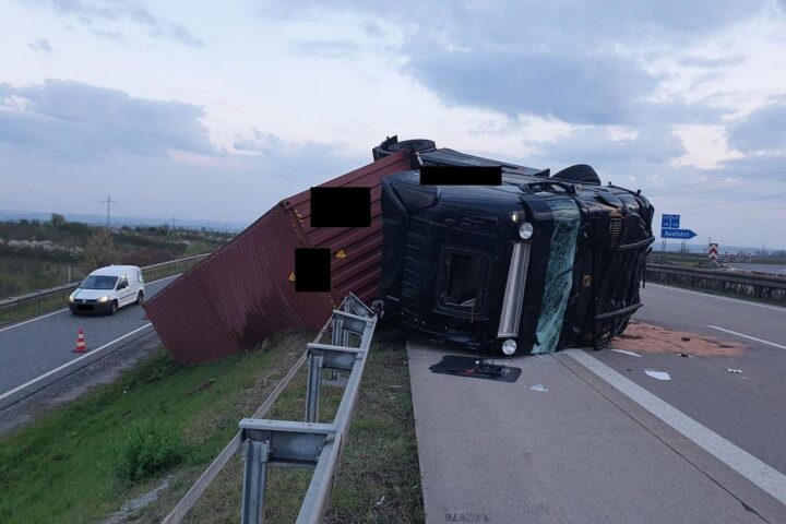 Sattelzug liegt umgekippt auf der Autobahn, Schutzleitplanke durchbrochen, Verkehr gesperrt.