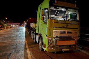 Überladener Schwertransporter mit Kabeltrommel und Stahlseil auf Autobahn Rastanlage.
