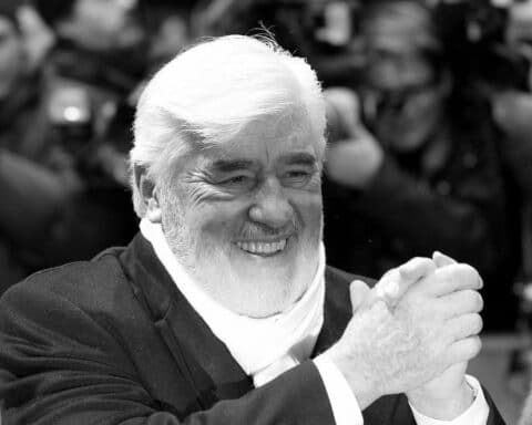 Mario Adorf, der legendäre Schauspieler, lächelnd in eleganter Kleidung, umgeben von Erinnerungen seiner Karriere.