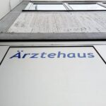 Ärztehaus mit Menschen, Symbol für Gesundheitsversorgung und Kritik an Kürzungen im Gesundheitssystem.