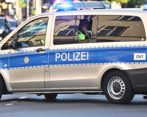Eingangstür eines Autoteilehändlers mit Einschusslöchern und Polizeiabsperrung in Neukölln.