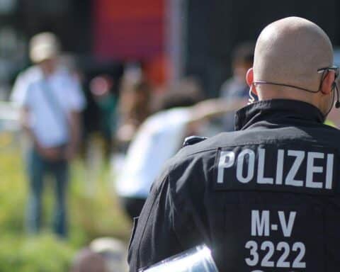 Ein verletzter Senior in einem Krankenfahrstuhl, Polizisten am Unfallort, Krankenwagen im Hintergrund.