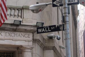 US-Börsen nach Zinsentscheid uneinheitlich - Goldpreis fällt Wallstreet mit steigenden Aktienkursen und Börsenschildern, US-Flaggen im Hintergrund.