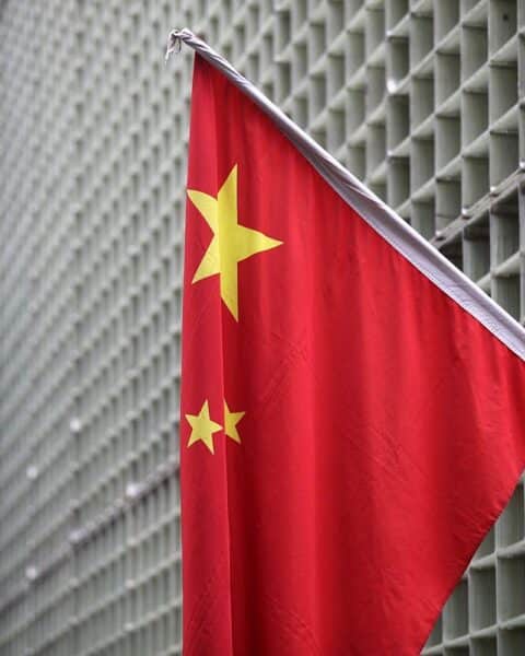 Chinesische Flagge vor industriellem Hintergrund, symbolisiert den Import seltener Erden nach Deutschland.