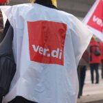 Demonstrierende Menschen am 1. Mai, Transparente für Arbeitnehmerrechte, starke Gewerkschaftsvertretung sichtbar.
