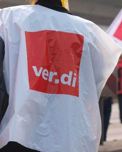 Demonstrierende Menschen am 1. Mai, Transparente für Arbeitnehmerrechte, starke Gewerkschaftsvertretung sichtbar.