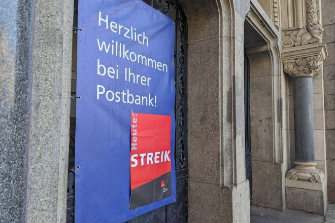 Streik-Hinweis an Postbank-Filiale, symbolisiert Forderungen nach besseren Arbeitsbedingungen und Gehältern.