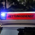 Ein Rettungswagen an einem Unfallort mit schwer beschädigtem Fahrzeug und verletzten Personen.