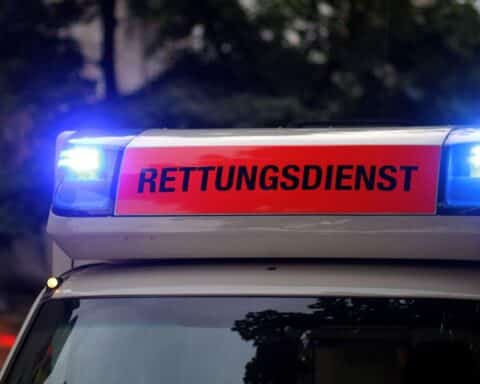 Ein Rettungswagen an einem Unfallort mit schwer beschädigtem Fahrzeug und verletzten Personen.