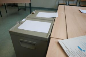 Wahllokal mit Wahlurnen und Wählern, Darstellung der aktuellen Wahlbeteiligung in Freiburg.