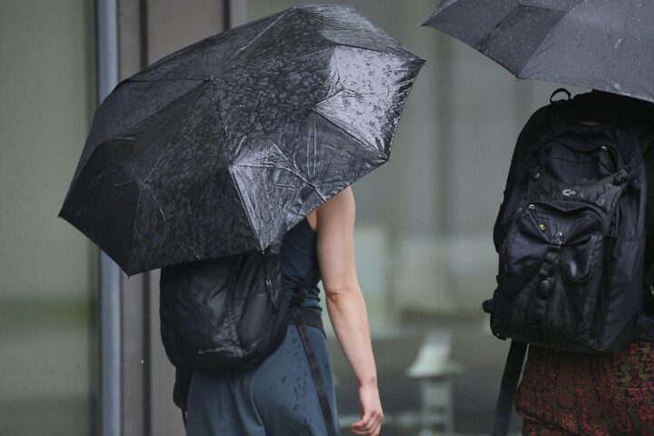 Nasser Regenschirm vor bewölktem Himmel, symbolisiert wechselhaftes Wetter mit Frost und Regen.