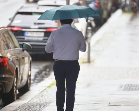 Mann mit Regenschirm in wechselhaftem Wetter, passend zum wechselnden Klima in Berlin.