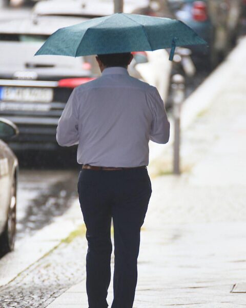 Mann mit Regenschirm in wechselhaftem Wetter, passend zum wechselnden Klima in Berlin.