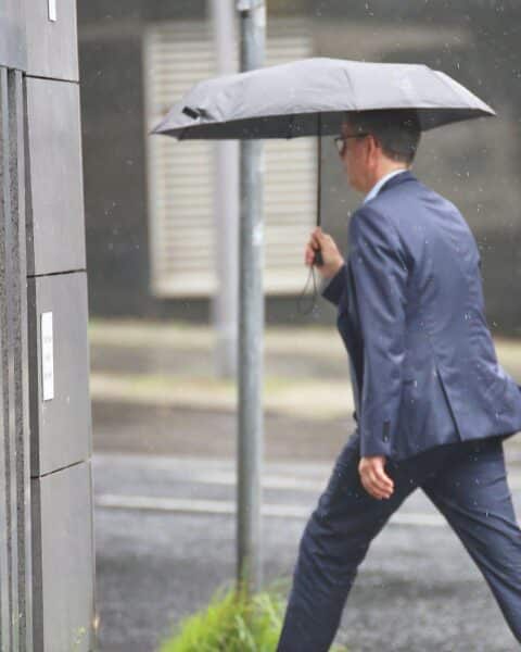 Mann mit Regenschirm unter bewölktem Himmel, symbolisiert wechselhaftes Wetter in Hessen.