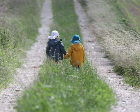 Zwei Kinder laufen auf einem Feldweg unter freundlichem Wetter mit Sonne und Wolken.